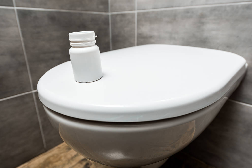 Behälter mit Pillen auf Keramik saubere Toilettenschüssel in moderner Toilette mit grauer Fliese - Foto, Bild