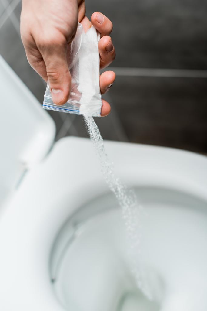vista recortada del hombre vertiendo cocaína en el inodoro en el baño moderno con baldosas grises
 - Foto, Imagen