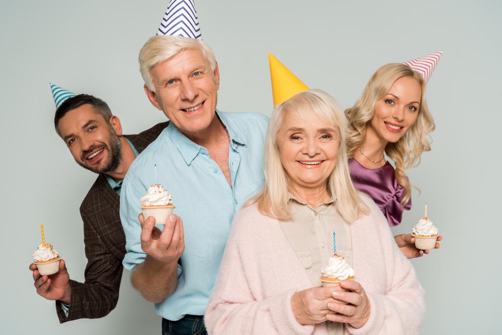 pais seniores felizes com filha adulta e filho segurando cupcakes de aniversário isolados em cinza
 - Foto, Imagem
