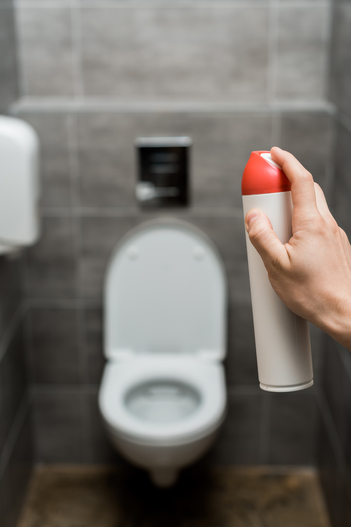vista ritagliata dell'uomo spruzzando deodorante per ambienti in bagno moderno con piastrelle grigie
 - Foto, immagini