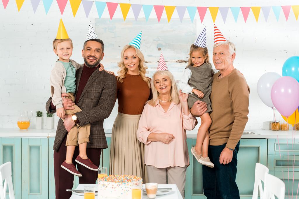 boldog család pózol a kamera, miközben áll közel születésnapi torta konyhaasztalon - Fotó, kép