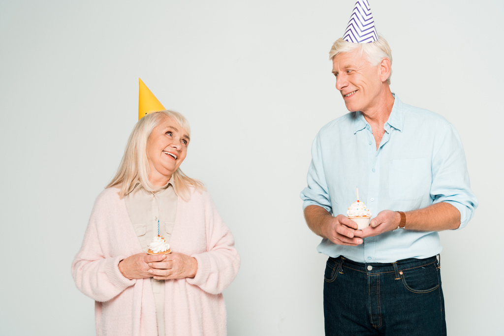 onnellinen vanhempi aviomies ja vaimo tilalla syntymäpäivä cupcakes ja etsivät toisiaan eristetty harmaa
 - Valokuva, kuva
