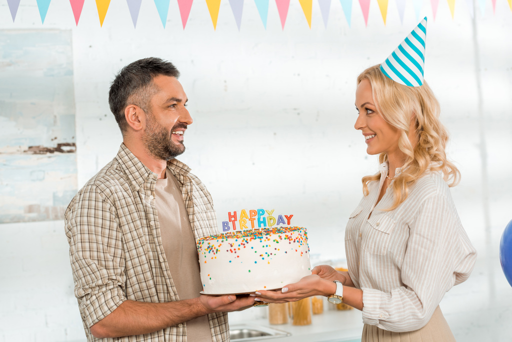 moglie sorridente che presenta la torta di compleanno con le candele di compleanno felici al marito
 - Foto, immagini