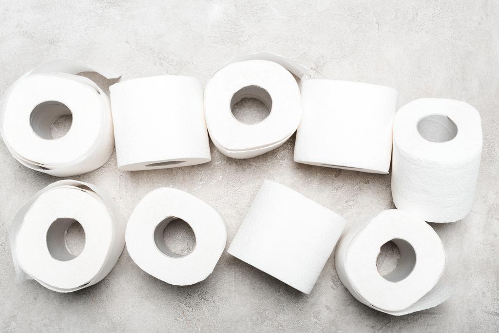 bovenaanzicht van rollen toiletpapier op grijs getextureerd oppervlak - Foto, afbeelding