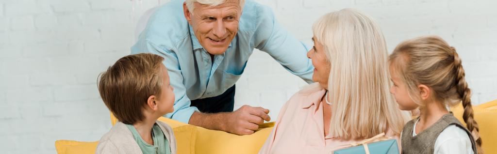 plano panorámico del hombre mayor hablando con la esposa feliz sentado en el sofá con nietos
 - Foto, imagen
