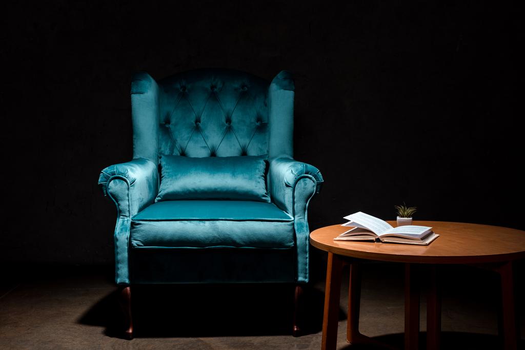 elegáns velúr kék fotel közel fa asztal könyv elszigetelt fekete - Fotó, kép