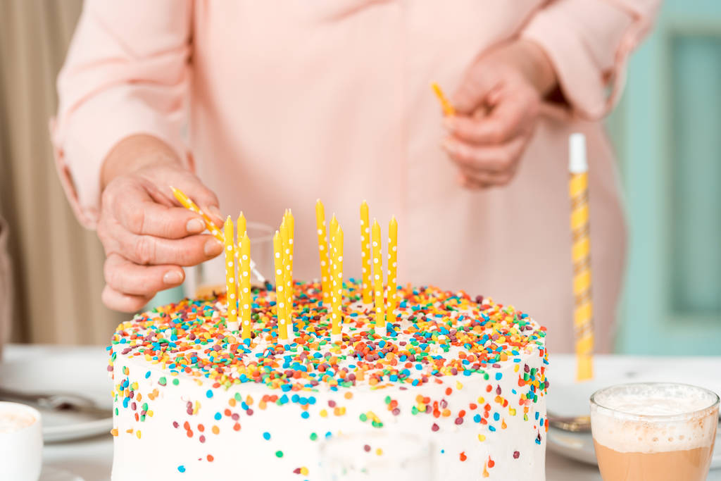 обрізаний вид на старшу жінку, що кладе свічки в смачний торт на день народження
 - Фото, зображення