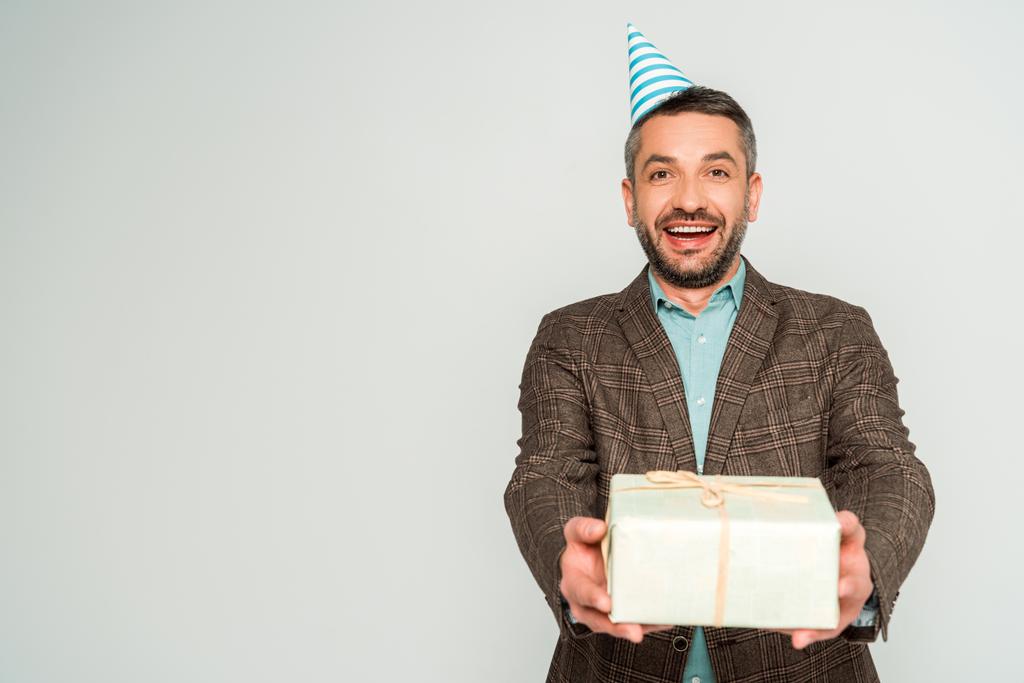 щасливий чоловік у вечірній шапці тримає подарункову коробку, дивлячись на камеру ізольовано на сірому
 - Фото, зображення