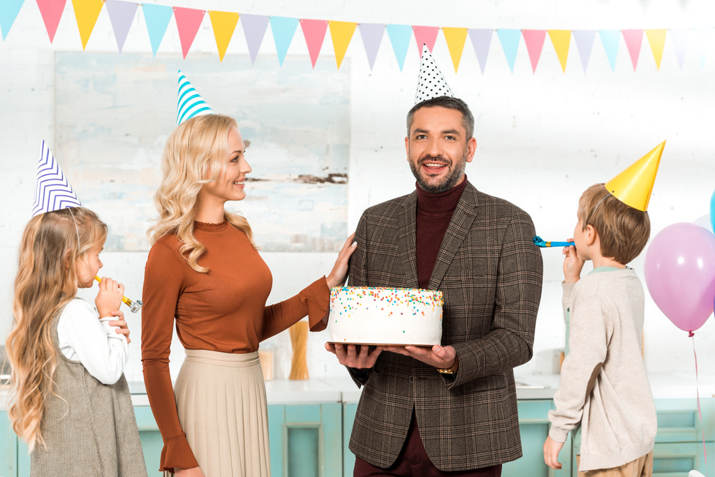 uomo felice guardando la fotocamera mentre tiene torta di compleanno vicino moglie e figli
 - Foto, immagini