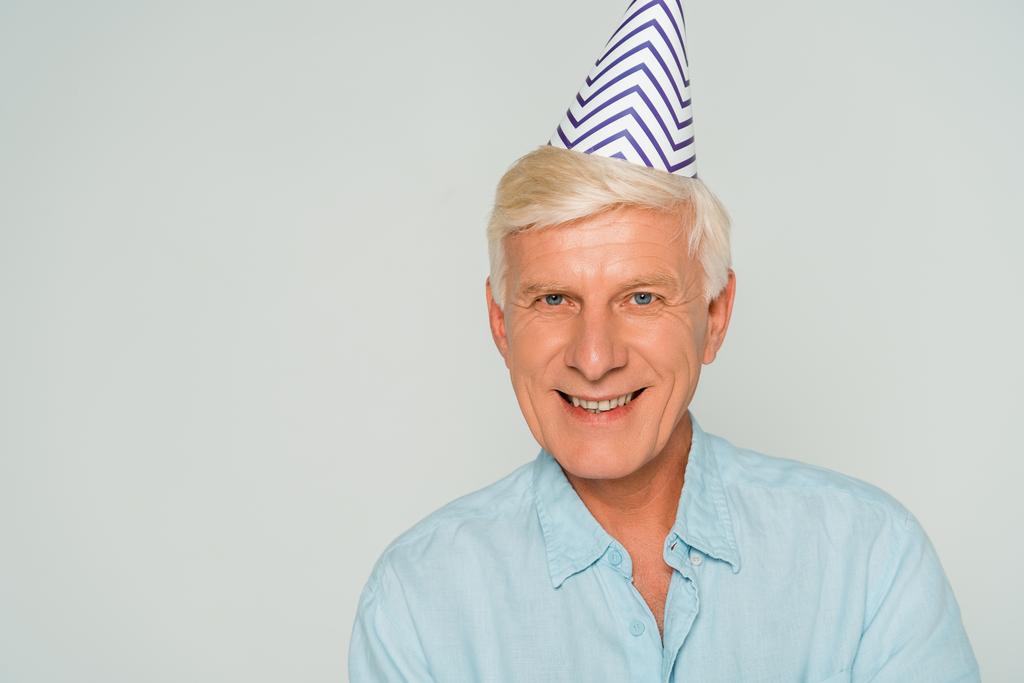happy senior man in party cap smiling at camera isolated on grey - Photo, Image
