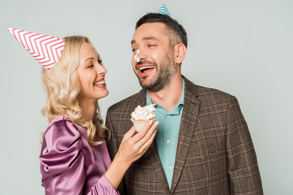 veselá žena drží narozeninový dortík v blízkosti usmívající se manžel se šlehačkou na nose izolované na šedé - Fotografie, Obrázek