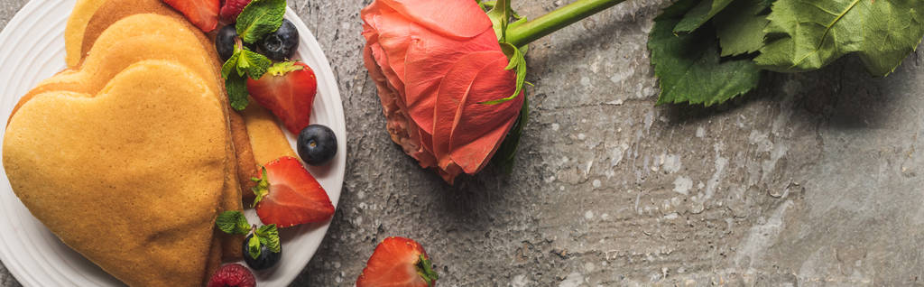 top view of heart shaped pancakes with fresh berries on grey concrete surface with rose, panoramic shot - 写真・画像
