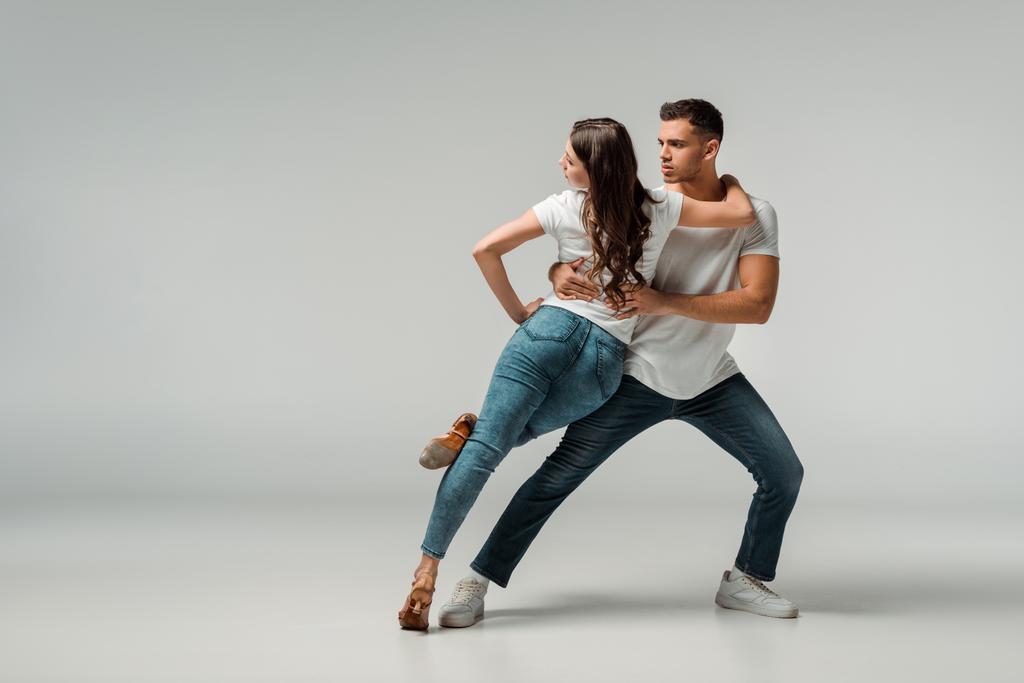 dansers in t-shirts en jeans dansen bachata op grijze achtergrond  - Foto, afbeelding