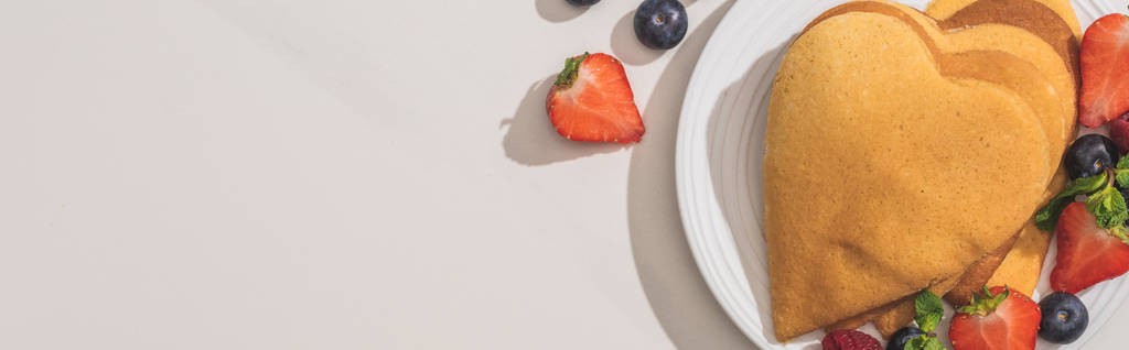 horní pohled na srdce tvarované palačinky s chutnými bobulemi na talíři na bílém pozadí, panoramatický výstřel - Fotografie, Obrázek