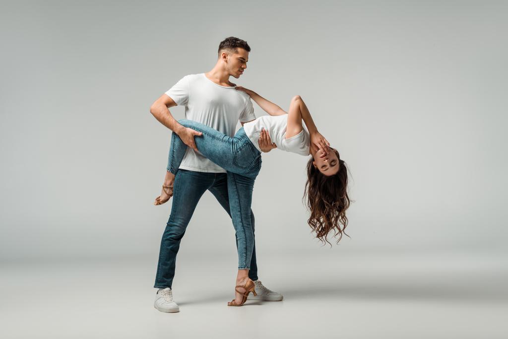 tanečníci v tričkách a džínách tančící bachata na šedém pozadí  - Fotografie, Obrázek