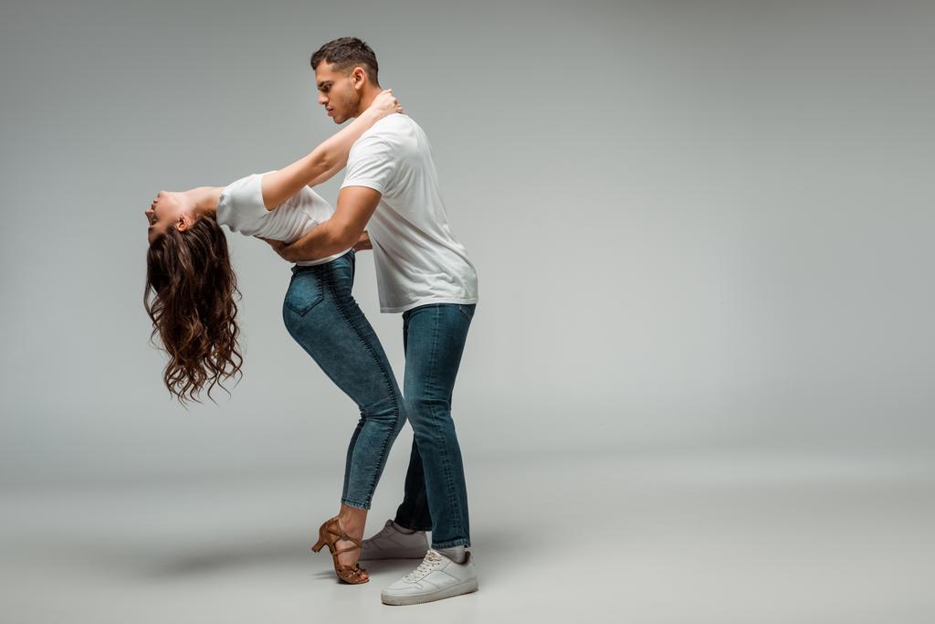 боковой вид танцоров в футболках и джинсах, танцующих бачату на сером фоне
  - Фото, изображение