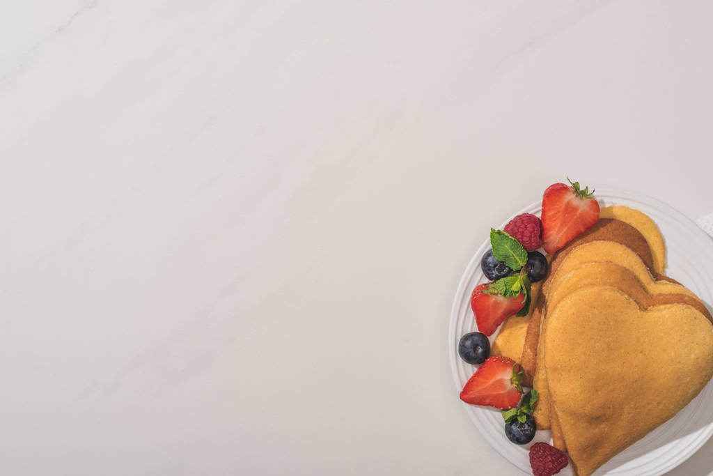 вид зверху смачні млинці у формі серця з ягодами та м'ятою на білому тлі
 - Фото, зображення