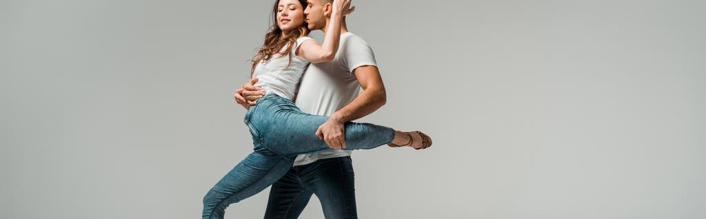 panoramiczne ujęcie uśmiechniętych tancerzy w t-shirtach i dżinsach tanecznych bachata izolowana na szarości   - Zdjęcie, obraz