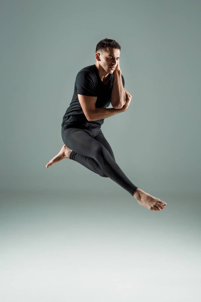 handsome dancer with closed eyes in black leggings and t-shirt dancing contemporary on dark background - Photo, Image