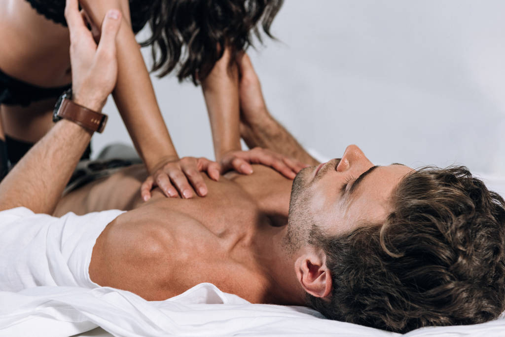 vista ritagliata di donna sexy sopra l'uomo senza maglietta sdraiato sul letto
 - Foto, immagini