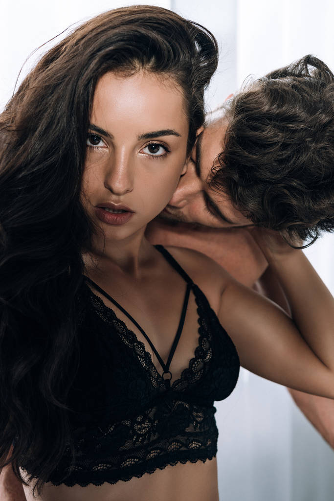 sexy Frau blickt in die Kamera, während ihr Freund ihren Hals küsst - Foto, Bild
