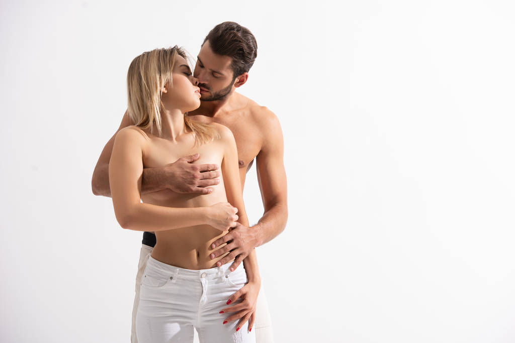 vášnivý muž líbání a zakrývání ňader své nahé přítelkyně, izolované na bílém - Fotografie, Obrázek