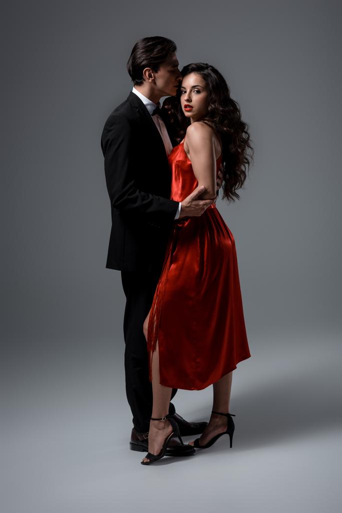 Романтична молода пара в костюмі і червона шовкова сукня обіймається на сірому
 - Фото, зображення