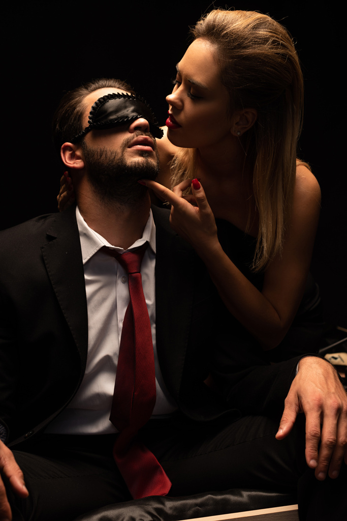 ελκυστική σέξι γυναίκα αγκαλιάζει τον άνδρα με μάσκα στο κρεβάτι στο σκοτεινό δωμάτιο - Φωτογραφία, εικόνα