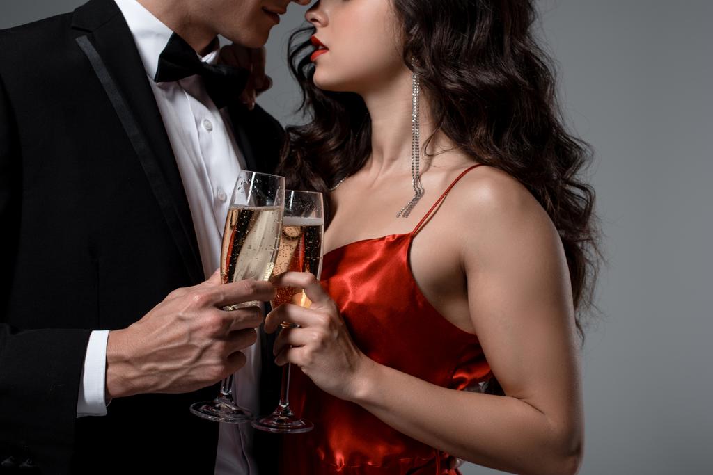 ostříhaný pohled na romantický pár objímající a držící sklenice šampaňského, izolované na šedi - Fotografie, Obrázek