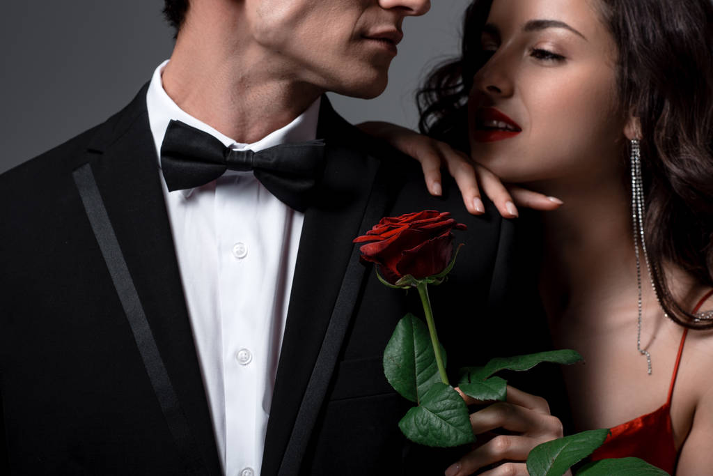 Coppia romantica che abbraccia e tiene il fiore di rosa rossa isolato sul grigio
 - Foto, immagini