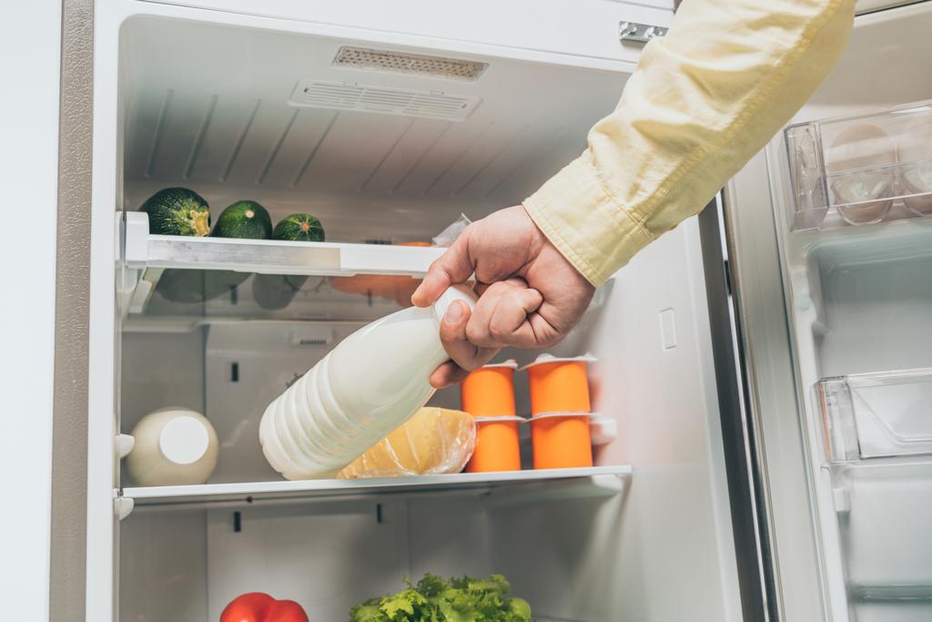 vista cortada do homem colocando garrafa de leite na geladeira com alimentos frescos nas prateleiras
 - Foto, Imagem