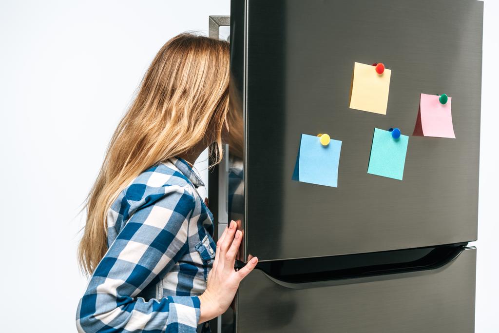 vrouw op zoek in open koelkast met plakkerige notities geïsoleerd op wit - Foto, afbeelding
