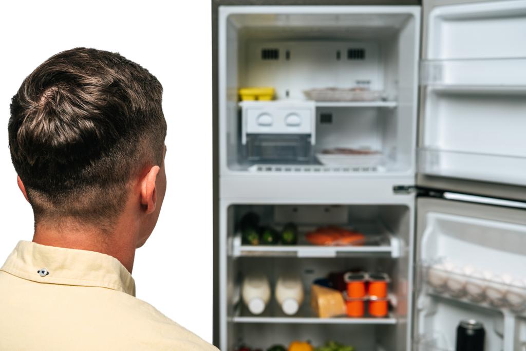 Mies katselee avointa jääkaappia ruoka eristettynä valkoiseen
 - Valokuva, kuva