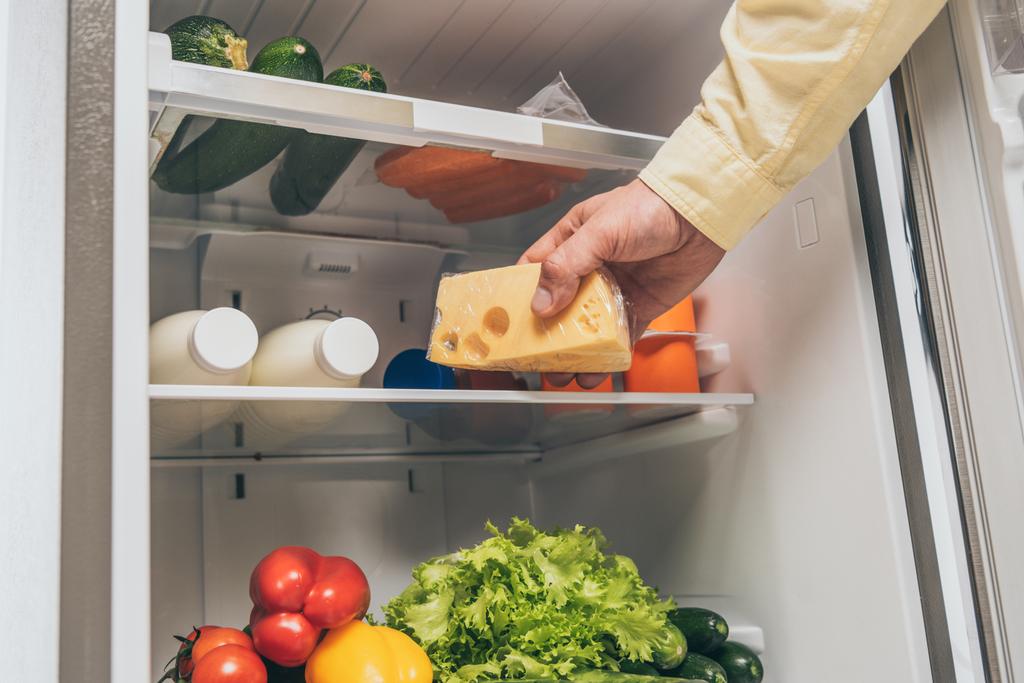abgeschnittene Ansicht eines Mannes, der Käse mit frischen Lebensmitteln aus dem Kühlschrank holt - Foto, Bild