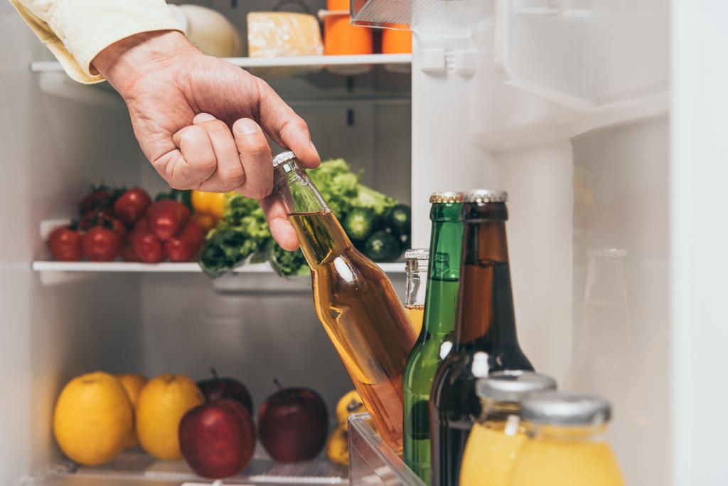 обрізаний вид чоловіка, який виймає пиво з холодильника зі свіжою їжею на полицях
 - Фото, зображення