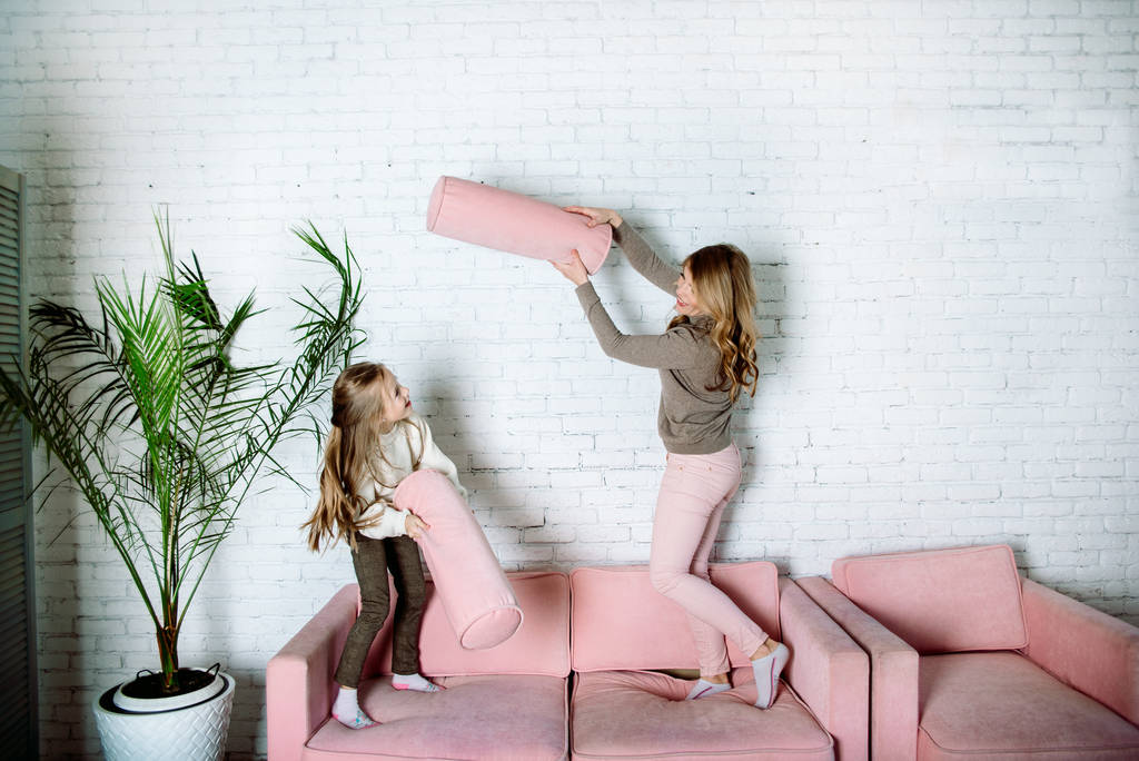 Parental love, upbringing and care.Happy mommy and kid daughter holding hands jumping on sofa together, baby sitter or mother playing fun with cute kid girl at home
 - Фото, изображение