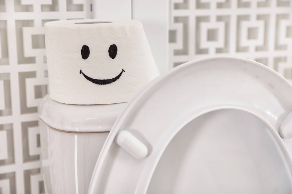 Papierrolle mit lustigem Gesicht auf Toilettentank im Badezimmer, Nahaufnahme - Foto, Bild