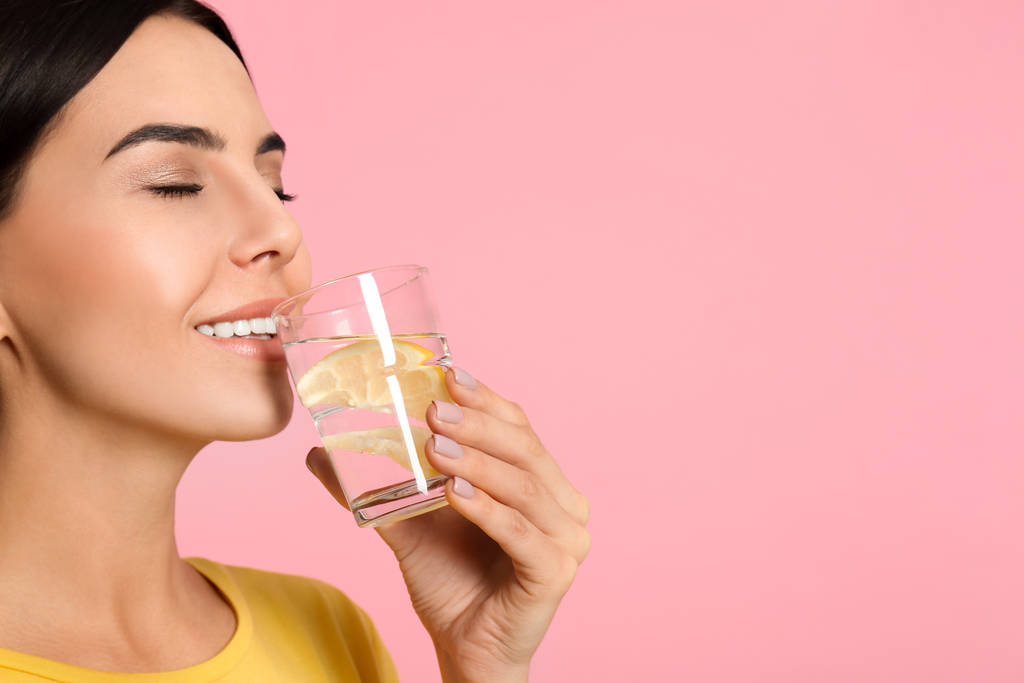 Gyönyörű fiatal nő iszik finom citromos víz rózsaszín backgro - Fotó, kép