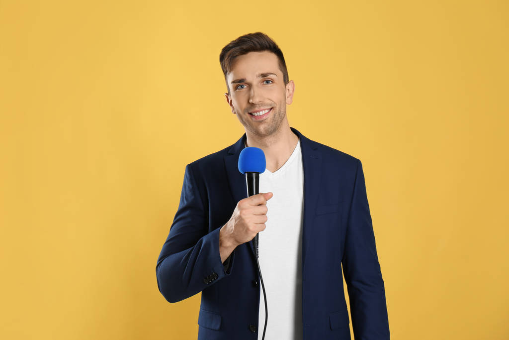 Joven periodista masculino con micrófono sobre fondo amarillo
 - Foto, Imagen