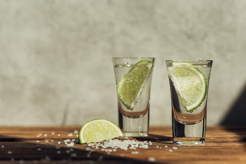 frischer Tequila mit Limette und Salz auf Holzoberfläche im Sonnenlicht - Foto, Bild