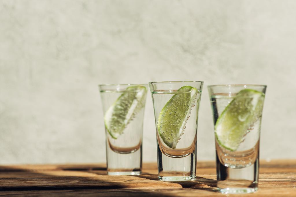 selective focus of fresh tequila with lime on wooden surface in sunlight - Photo, Image