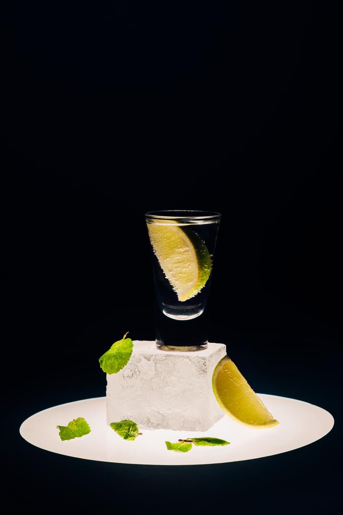 fresh tequila with lime and mint on ice cube on illuminated circle isolated on black - Photo, Image
