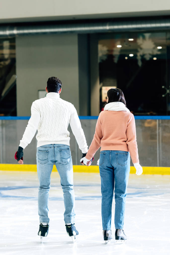 Rückansicht eines jungen Paares, das sich auf der Eisbahn an den Händen hält  - Foto, Bild