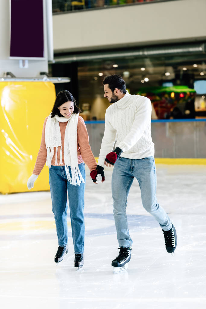 alegre jovem casal de mãos dadas e patinação na pista
  - Foto, Imagem