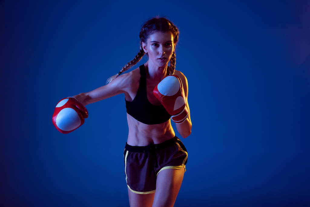 Ajuste mujer caucásica en el boxeo de ropa deportiva en fondo estudio azul en luz de neón
 - Foto, Imagen