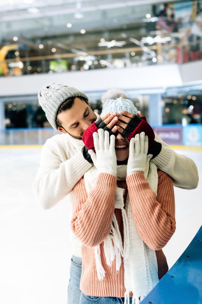 vrolijk man sluiten ogen naar vrouw naar maken een verrassing op schaatsbaan - Foto, afbeelding
