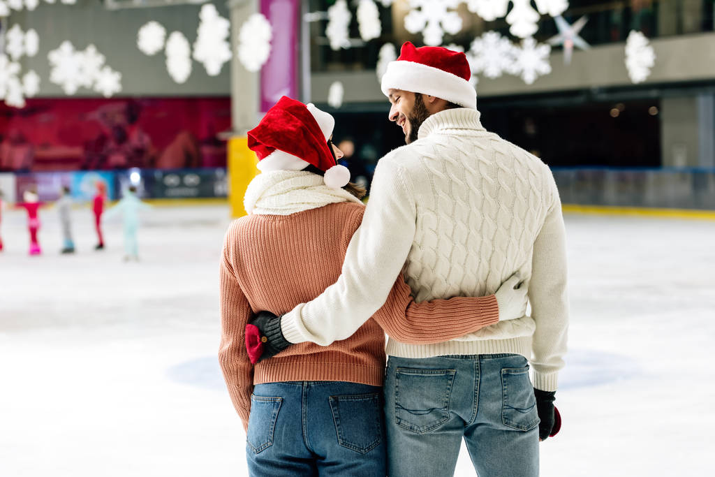 Noel Baba şapkalı mutlu çiftin paten sahasında birbirlerine sarılıp baktıkları arka plan görüntüsü. - Fotoğraf, Görsel