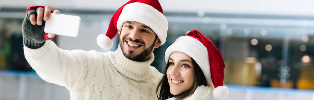 plan panoramique de couple heureux dans chapeaux Santa prendre selfie sur smartphone sur patinoire
 - Photo, image