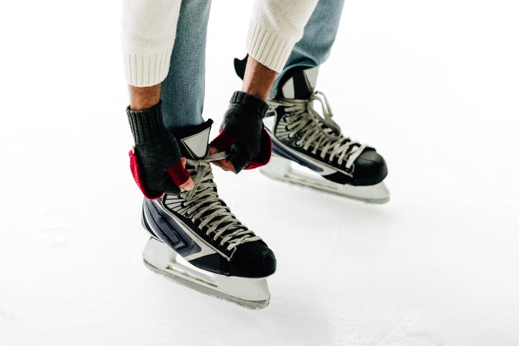 cropped view of man tying shoelaces of skates on skating rink - 写真・画像