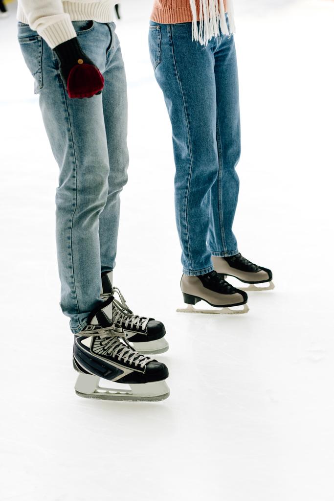 cropped view of young couple in jeans and skates standing on skating rink   - 写真・画像